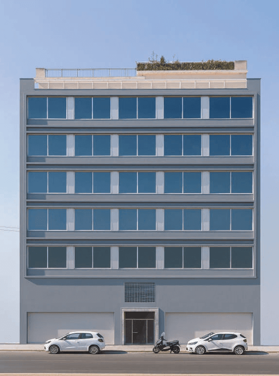 Building facade with horizontal rows of windows, an entrance door and the street in front.
